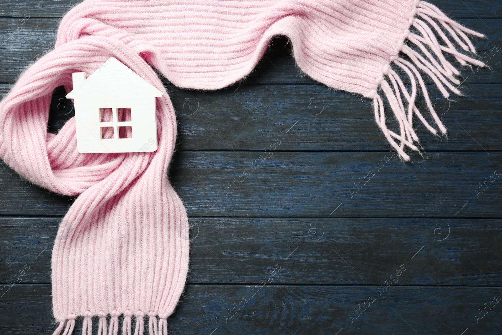 Photo of House model and pink scarf on dark blue wooden background, top view with space for text. Heating efficiency