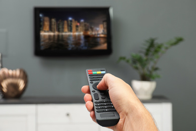 Image of Man switching channels on TV set with remote control at home