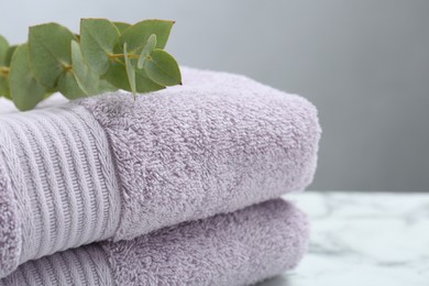 Photo of Violet terry towels and eucalyptus branch on table, closeup
