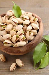 Photo of Delicious pistachios in bowl on wooden table, closeup