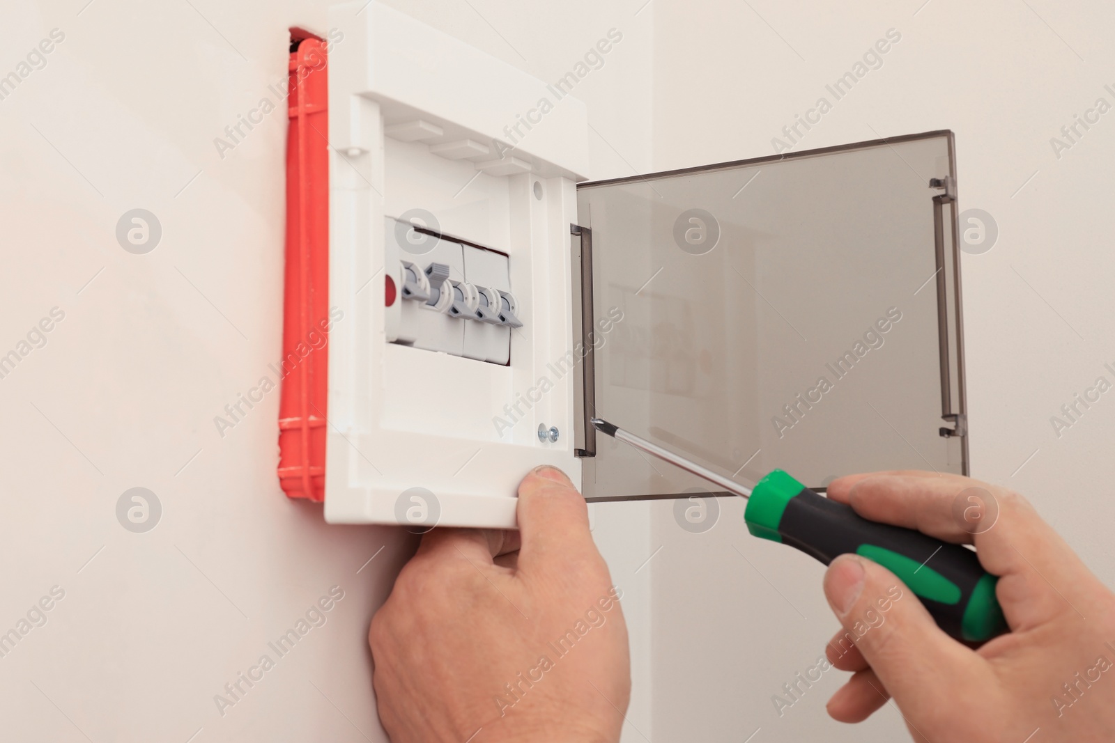 Photo of Electrician with screwdriver installing switchboard on wall indoors, closeup