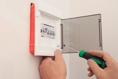 Photo of Electrician with screwdriver installing switchboard on wall indoors, closeup