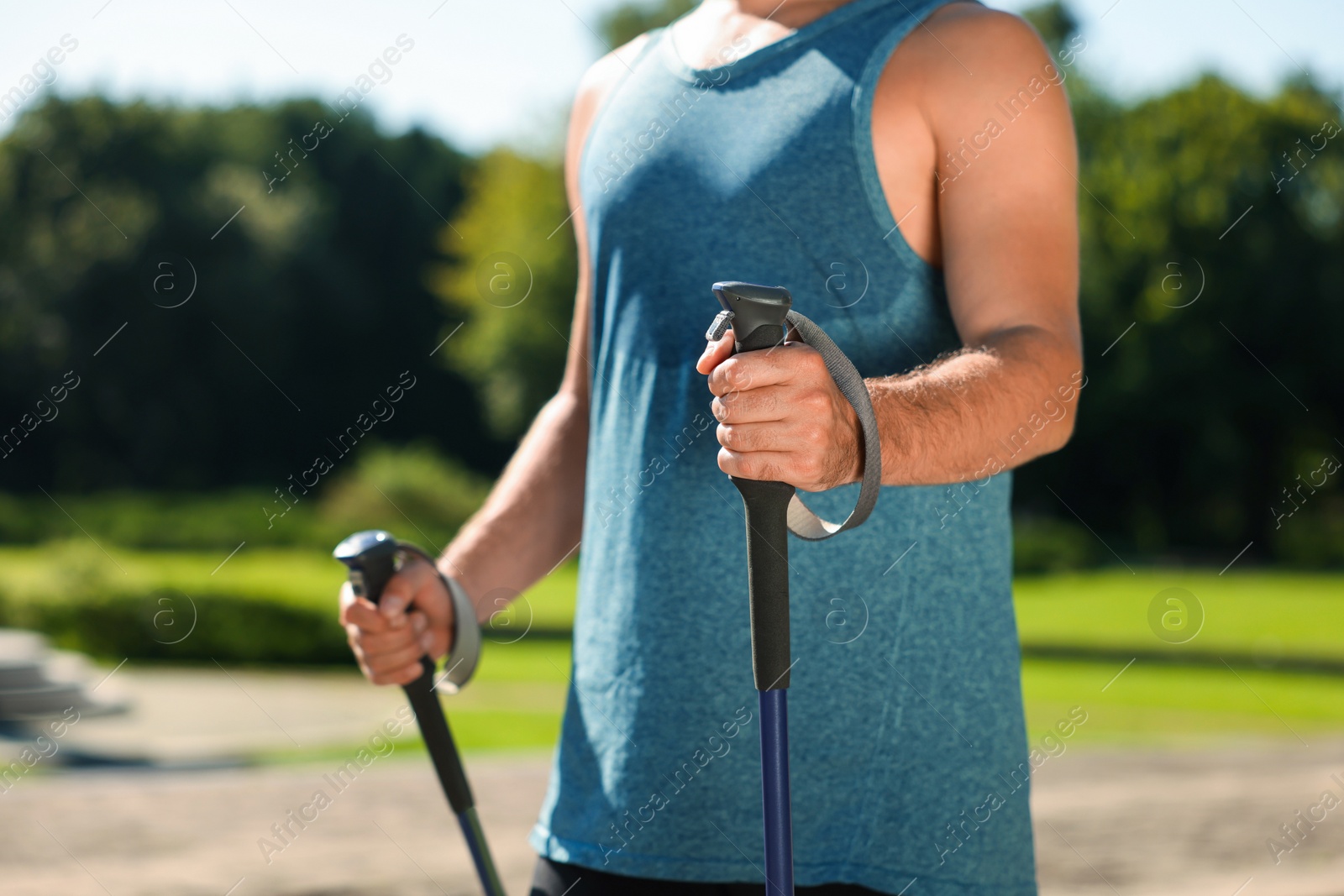 Photo of Man practicing Nordic walking with poles in park on sunny day, closeup