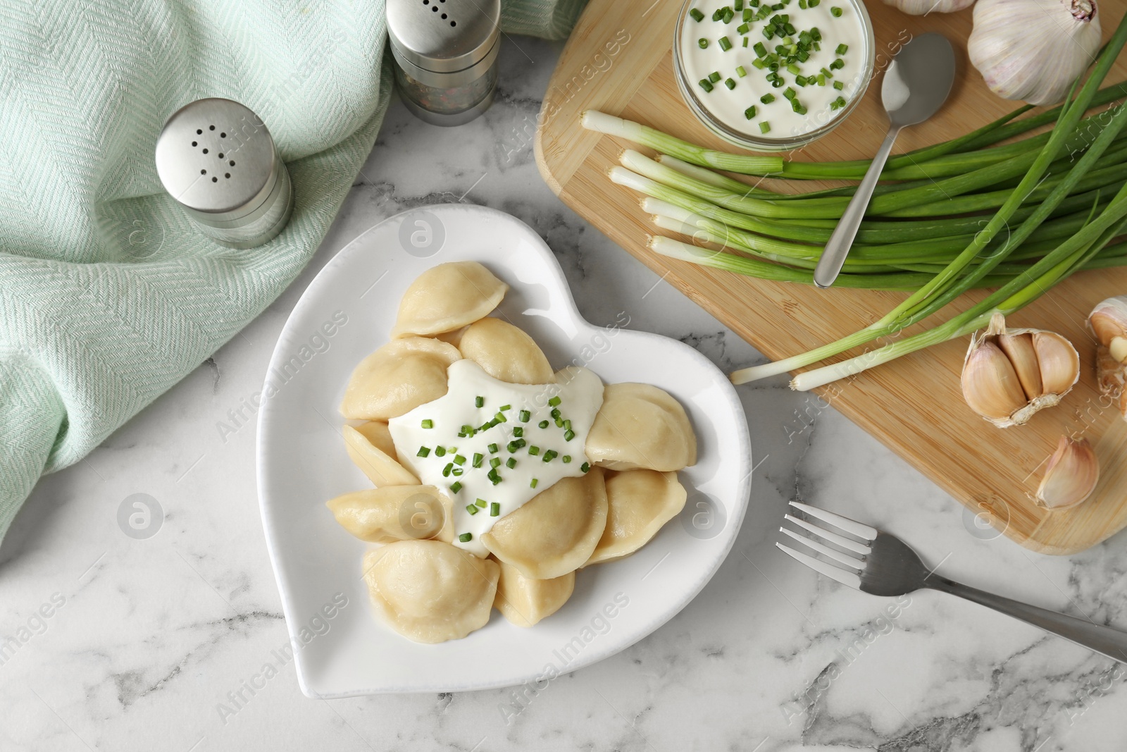 Photo of Delicious cooked dumplings with sour cream on white marble table, flat lay