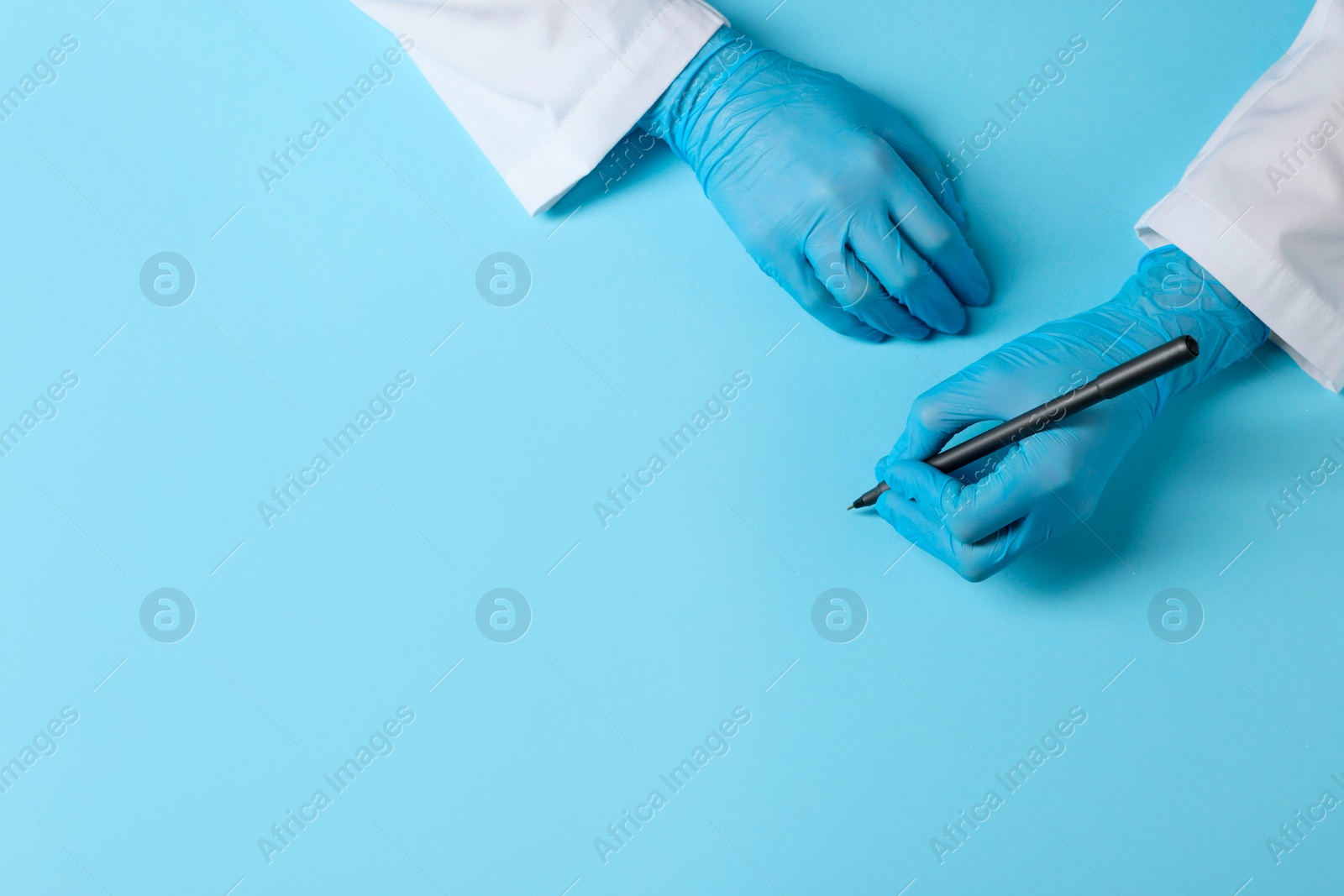 Photo of Doctor wearing medical gloves writing something on light blue background, top view. Space for text