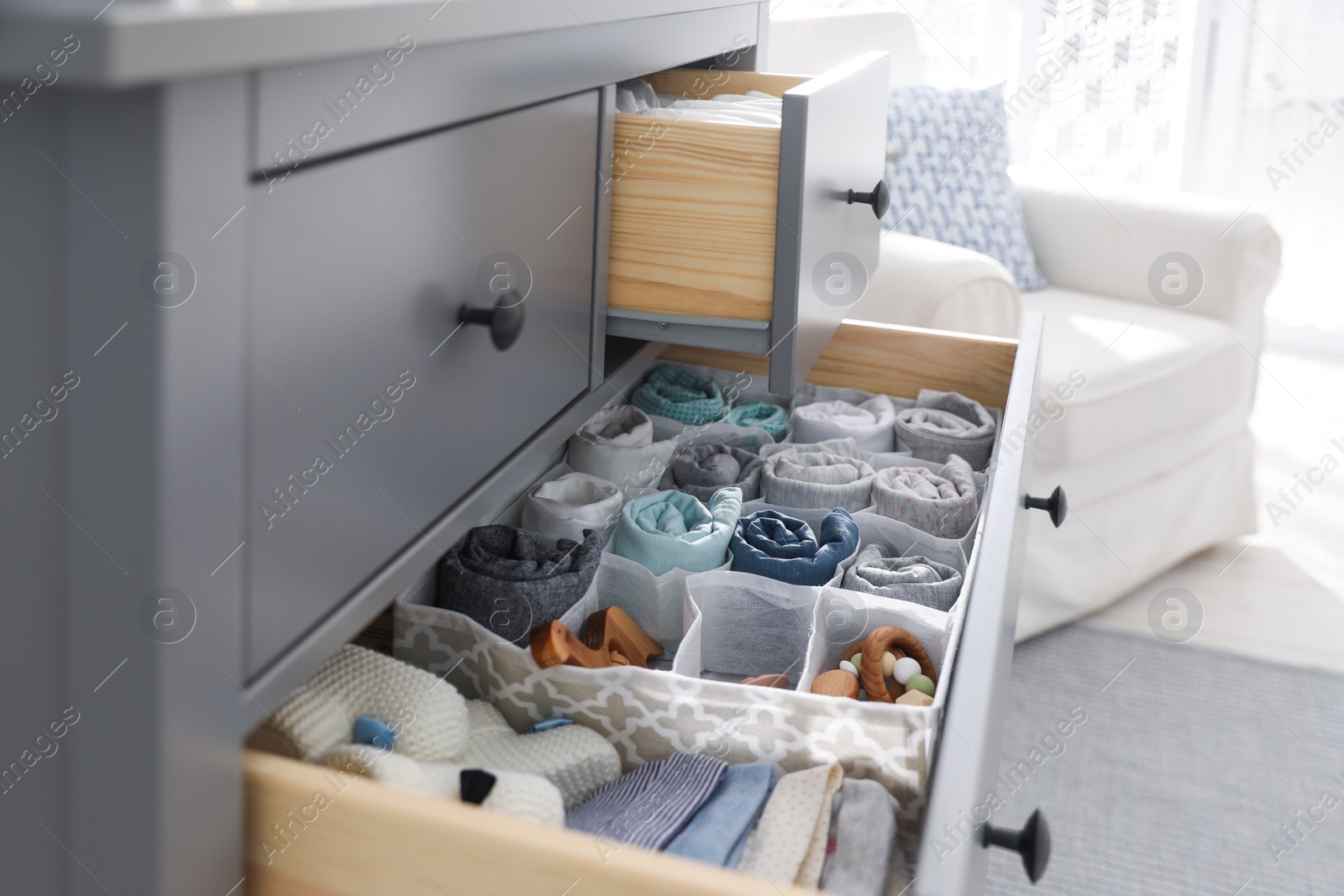 Photo of Modern open chest of drawers with baby clothes and accessories in room, closeup