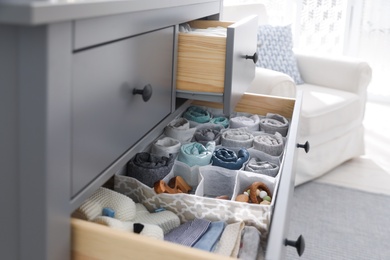 Modern open chest of drawers with baby clothes and accessories in room, closeup