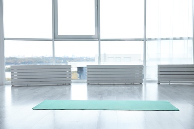 Photo of Unrolled light blue yoga mat on floor in room