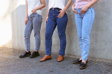 Photo of Women in stylish jeans near grey wall outdoors, closeup