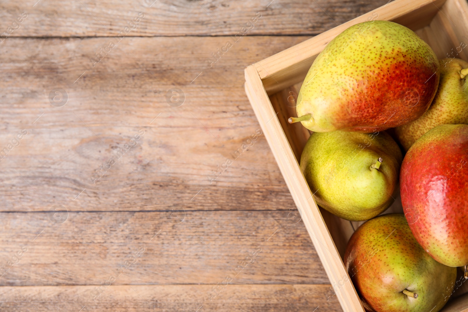 Photo of Crate with ripe juicy pears on brown wooden table, flat lay. Space for text