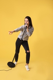 Young woman wearing casual clothes singing in microphone on color background