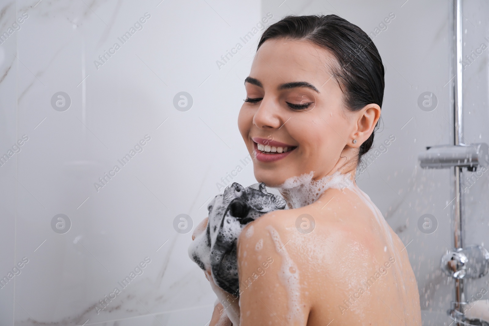 Photo of Young woman with mesh pouf taking shower at home. Space for text