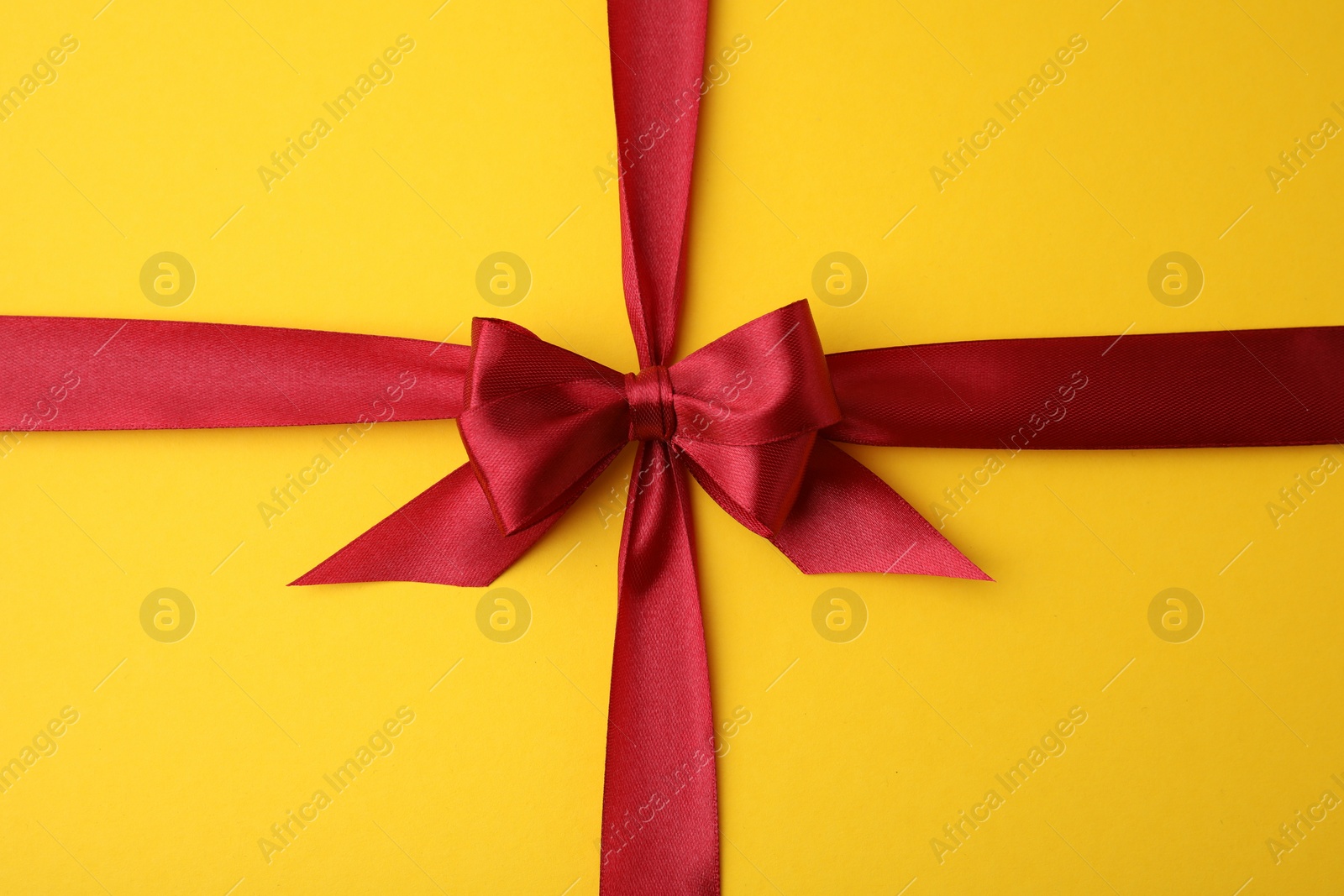 Photo of Red satin ribbon with bow on yellow background, top view