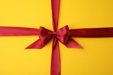 Photo of Red satin ribbon with bow on yellow background, top view