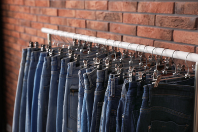 Photo of Rack with stylish jeans near brick wall, closeup
