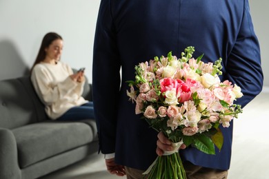 Man hiding bouquet of flowers for his beloved woman indoors, closeup