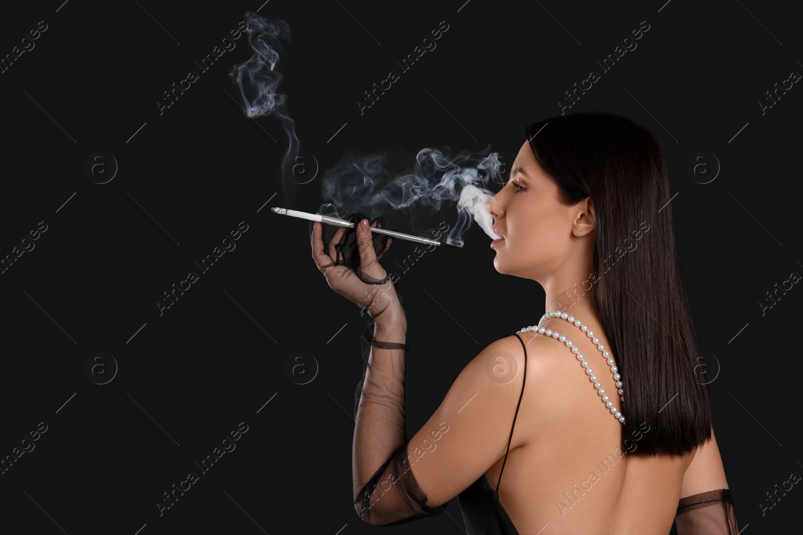 Photo of Woman using long cigarette holder for smoking on black background, space for text