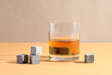 Photo of Whiskey stones and drink in glass on orange table, closeup