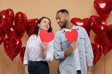 Photo of Lovely couple with red paper hearts on beige background. Valentine's day celebration