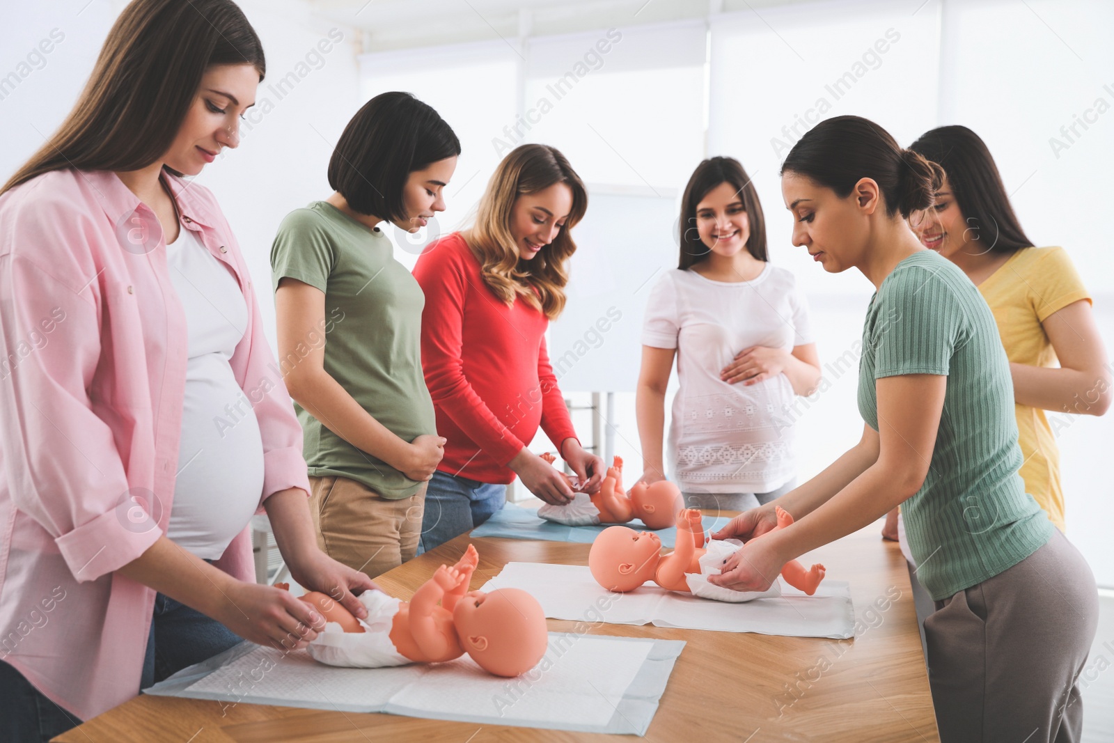 Photo of Pregnant women learning how to swaddle baby at courses for expectant mothers indoors