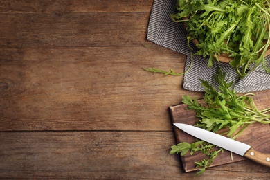 Fresh arugula, cutting board and knife on wooden table, flat lay. Space for text