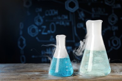 Laboratory glassware with colorful liquids and steam on wooden table against black background, space for text. Chemical reaction