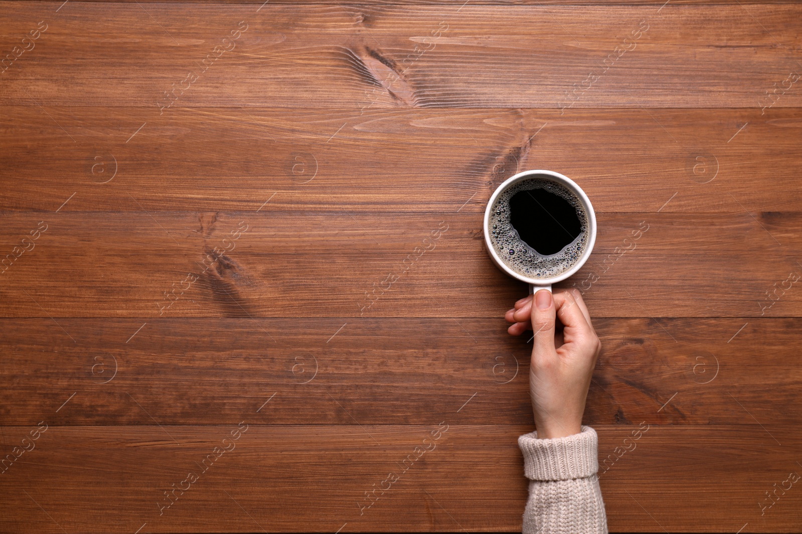 Photo of Woman with cup of coffee at wooden table, top view. Space for text