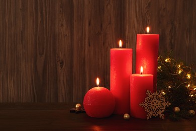 Photo of Beautiful burning candles with Christmas decor on wooden table, space for text