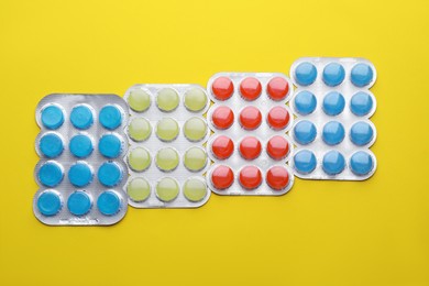 Photo of Blisters with colorful cough drops on yellow background, flat lay