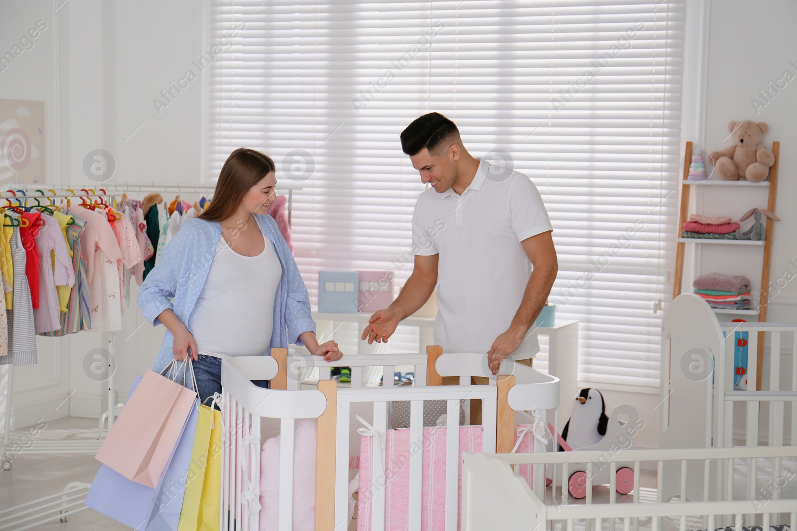 Photo of Happy pregnant woman and her husband with shopping bags choosing crib in store