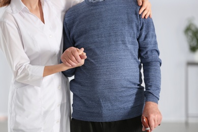 Photo of Elderly man with walking cane and female caregiver on blurred background, closeup