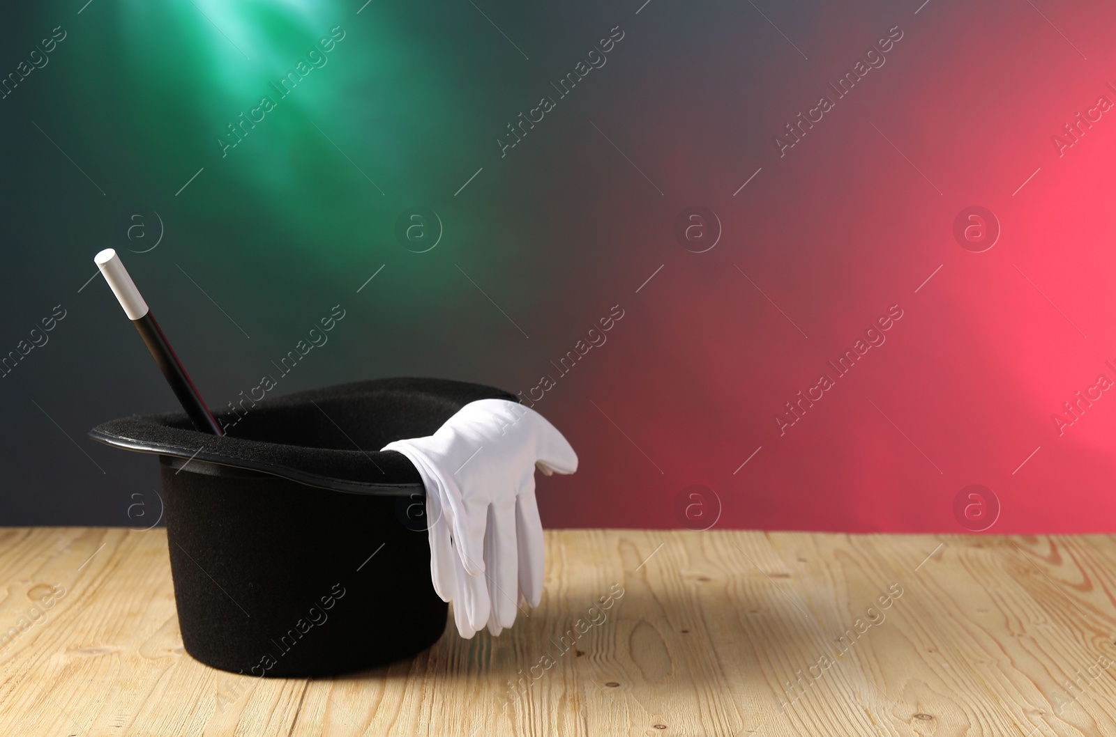 Photo of Magician's hat, wand and gloves on wooden table against color background, space for text