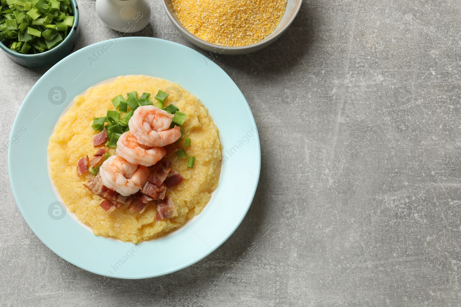 Photo of Plate with fresh tasty shrimps, bacon, grits and green onion on grey table, flat lay. Space for text