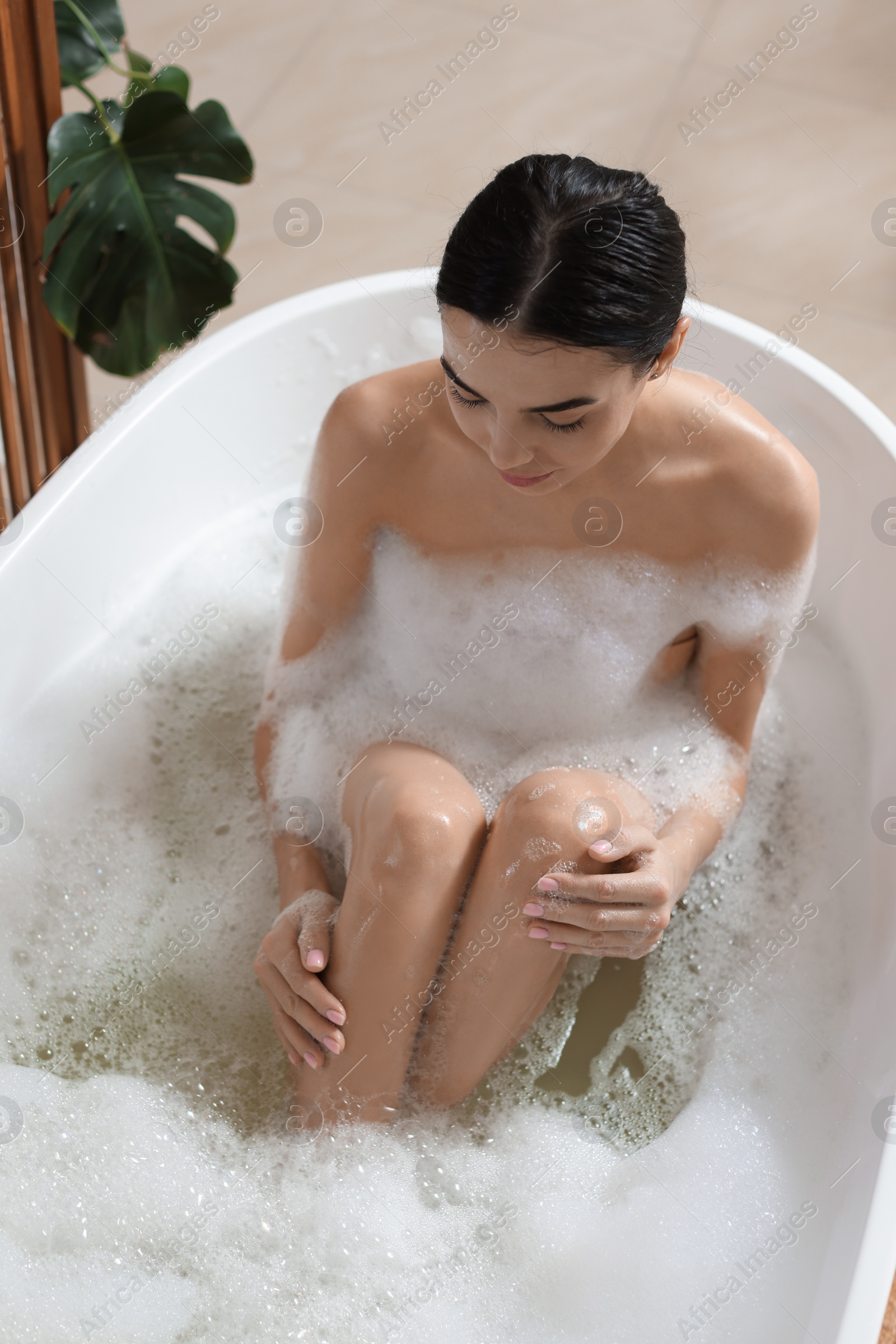 Photo of Beautiful young woman taking bubble bath at home, above view