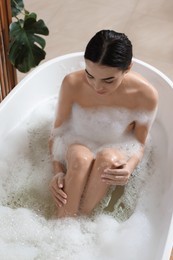 Beautiful young woman taking bubble bath at home, above view