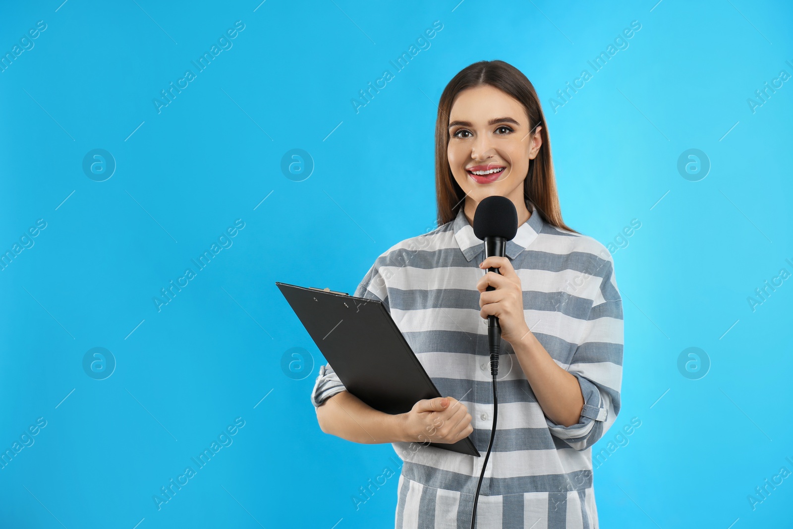 Photo of Young female journalist with microphone and clipboard on blue background