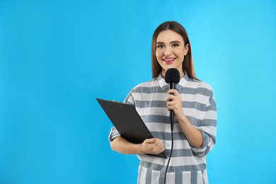 Young female journalist with microphone and clipboard on blue background