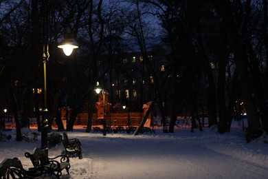Photo of Trees, street lamp and pathway covered with snow in evening park
