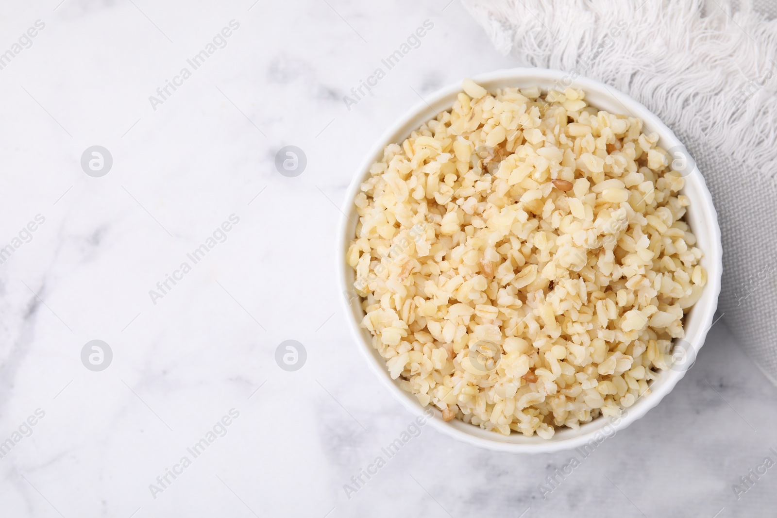 Photo of Cooked bulgur in bowl on white marble table, top view. Space for text