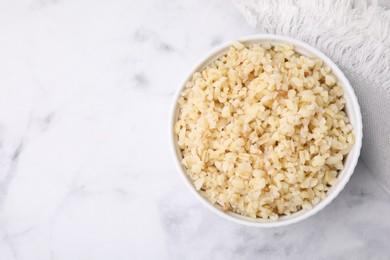 Cooked bulgur in bowl on white marble table, top view. Space for text