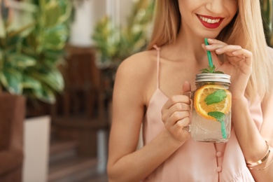 Young woman with mason jar of tasty natural lemonade in cafe, closeup. Detox drink