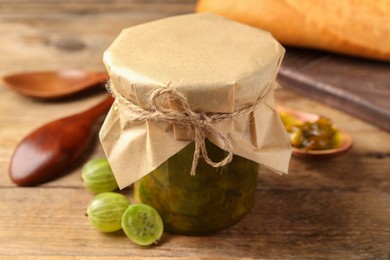 Jar of delicious gooseberry jam and fresh berries on wooden table, closeup