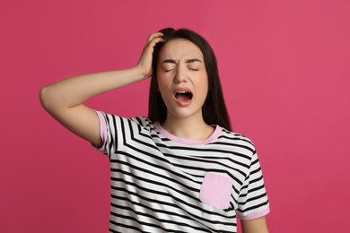 Young tired woman yawning on pink background