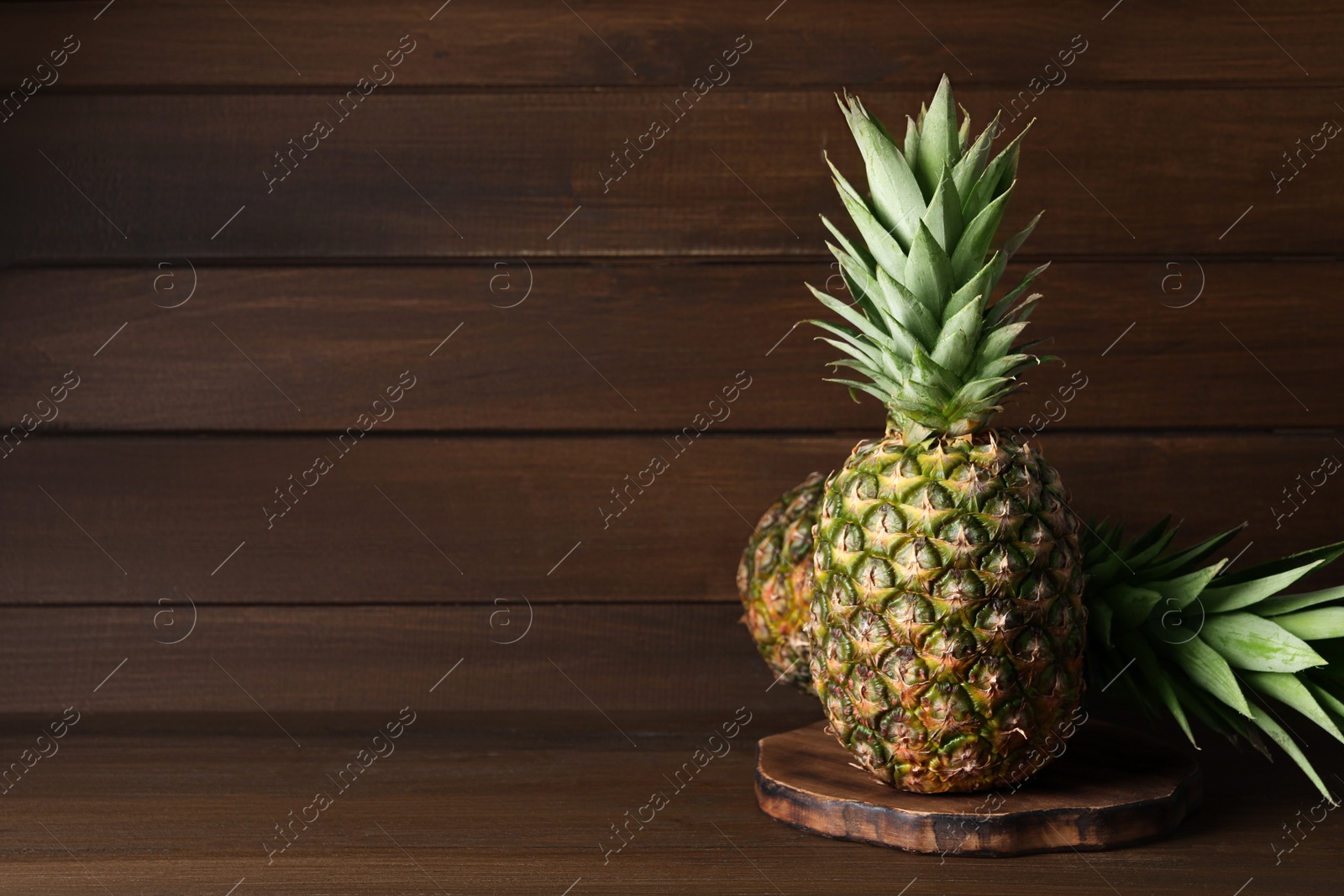 Photo of Whole ripe pineapples on wooden table, space for text