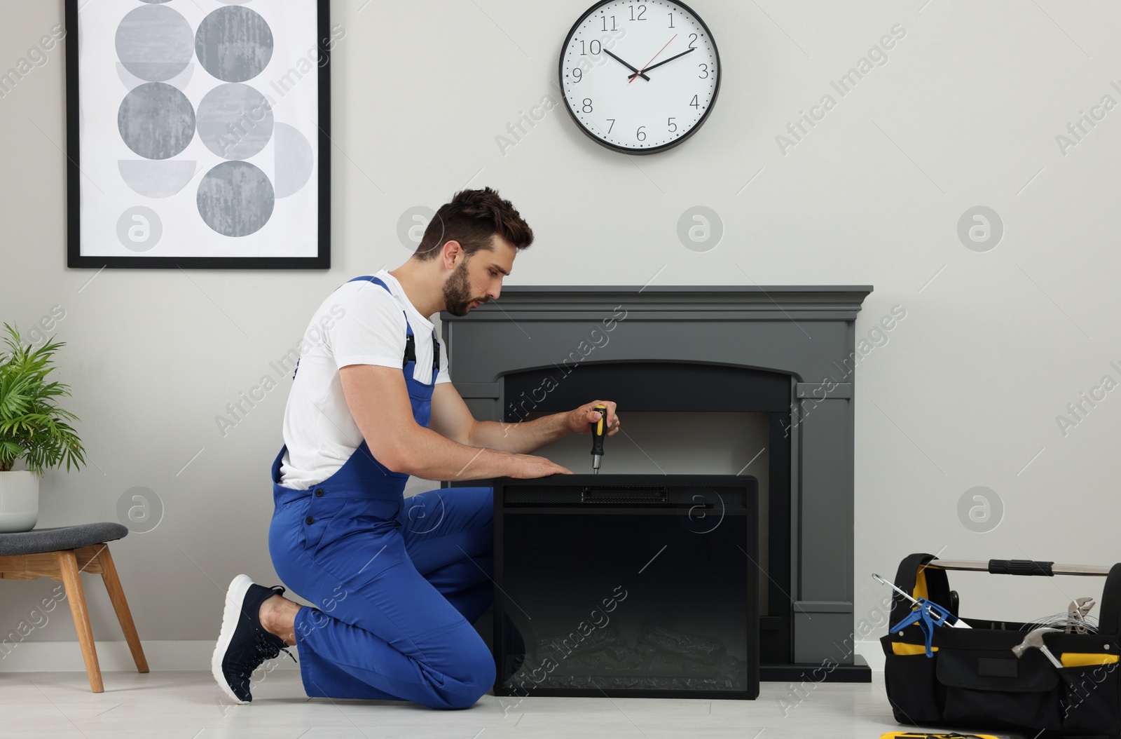 Photo of Professional technician with screwdriver installing electric fireplace in room