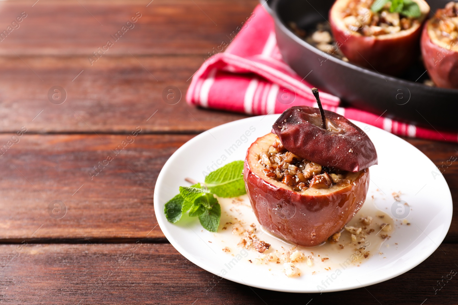 Photo of Tasty baked apples with nuts, honey and mint in dishware on wooden table, closeup. Space for text