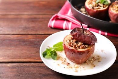 Tasty baked apples with nuts, honey and mint in dishware on wooden table, closeup. Space for text