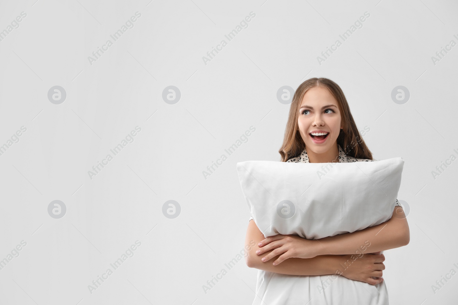 Photo of Beautiful woman with pillow on light grey background, space for text. Bedtime