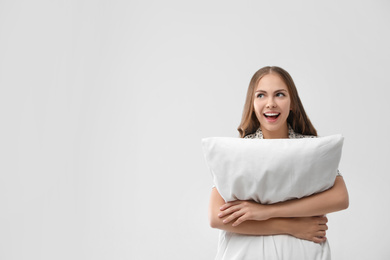 Photo of Beautiful woman with pillow on light grey background, space for text. Bedtime