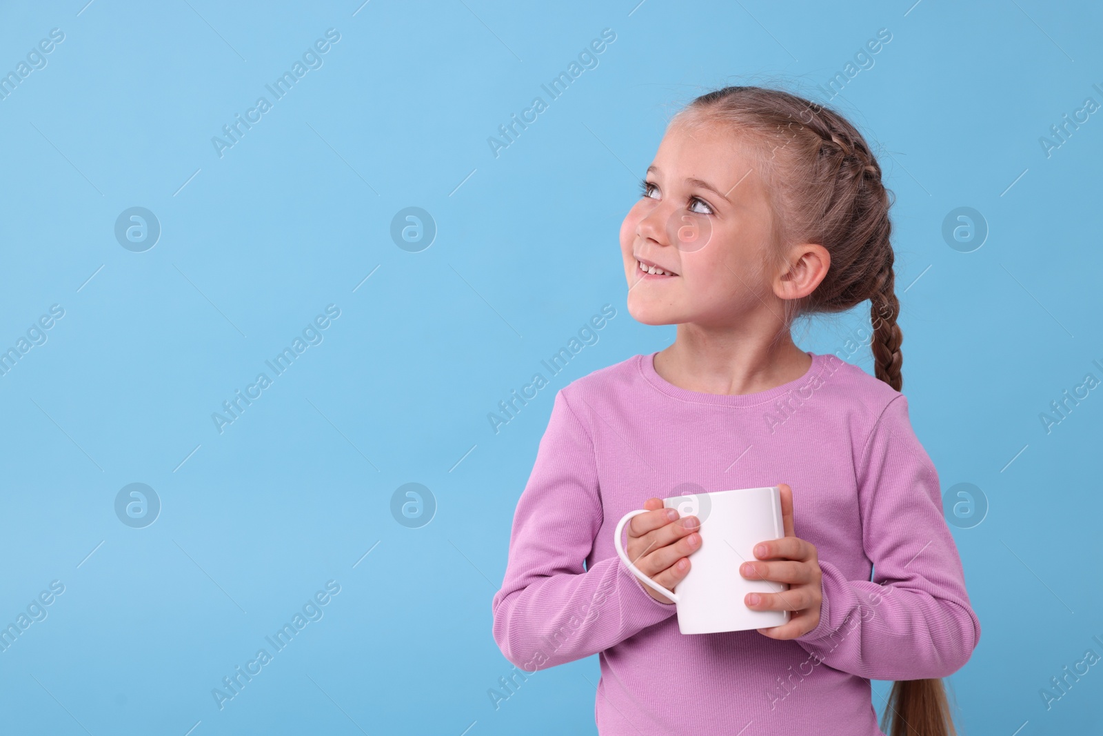 Photo of Happy girl with white ceramic mug on light blue background, space for text